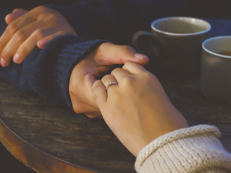 Một cặp đôi tin tưởng mạnh mẽ trong một mối quan hệ, cùng nắm tay nhau ngồi trên bàn.